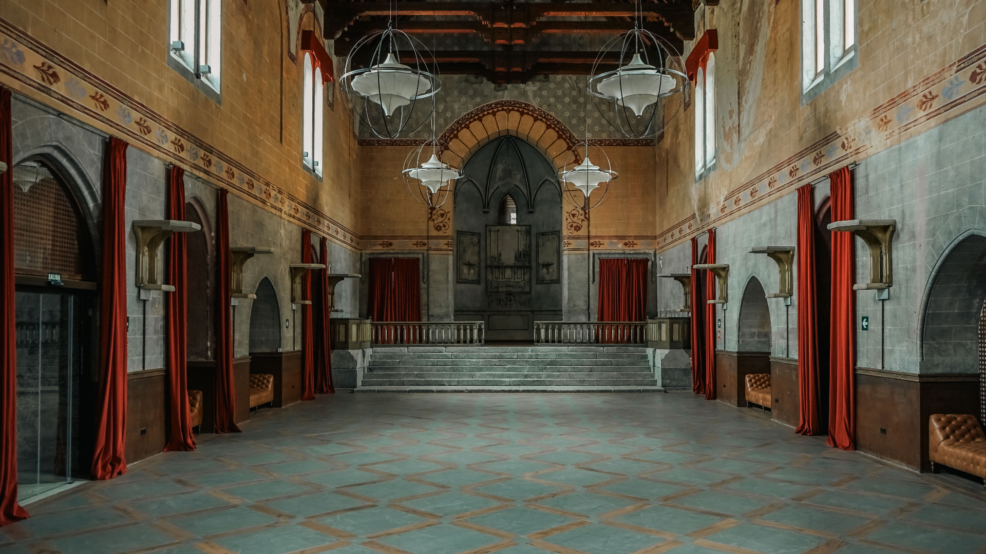 Sala histórica con arcos, cortinas rojas y lámparas esféricas