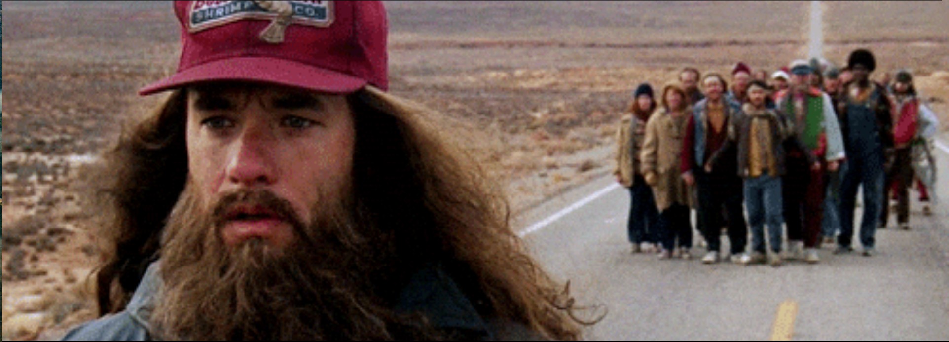 Forrest Gump corriendo por una carretera seguido por un grupo de caminantes